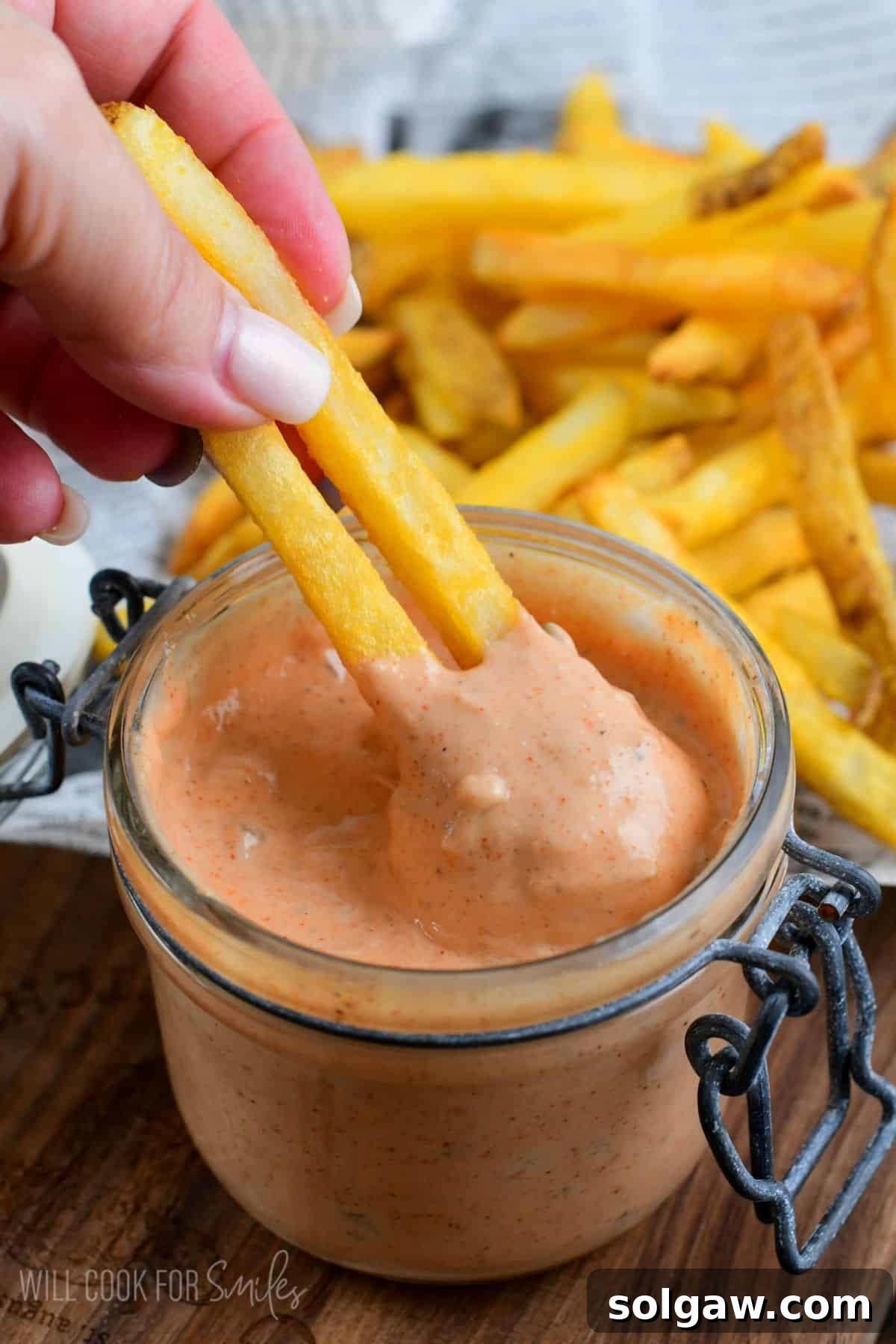 dipping two fried into a jar of burger sauce.