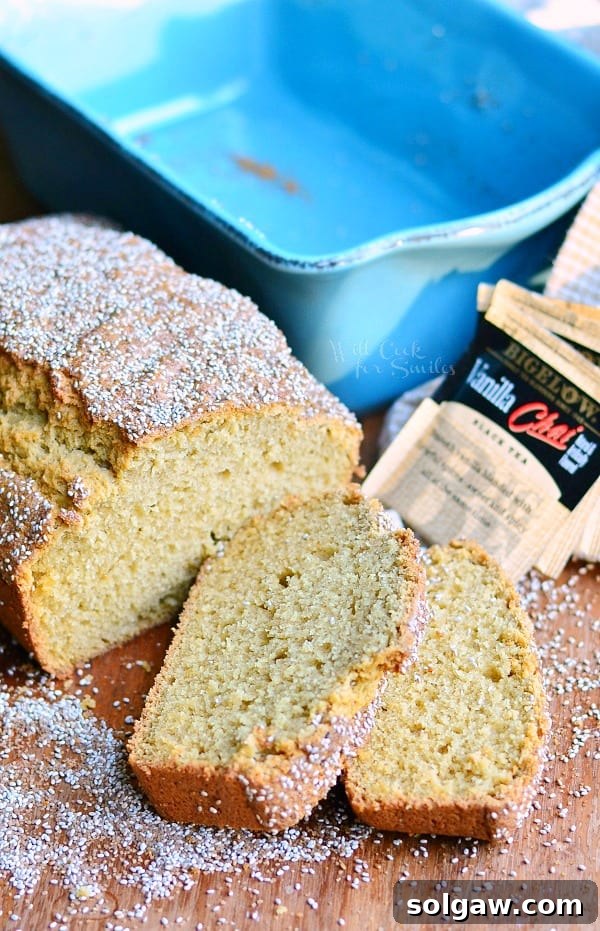 2 slices of vanilla chai tea bread cut from loaf laying on a wooden table with the rest of loaf behind and a blue baking dish in background with tea bags laying on tan cloth