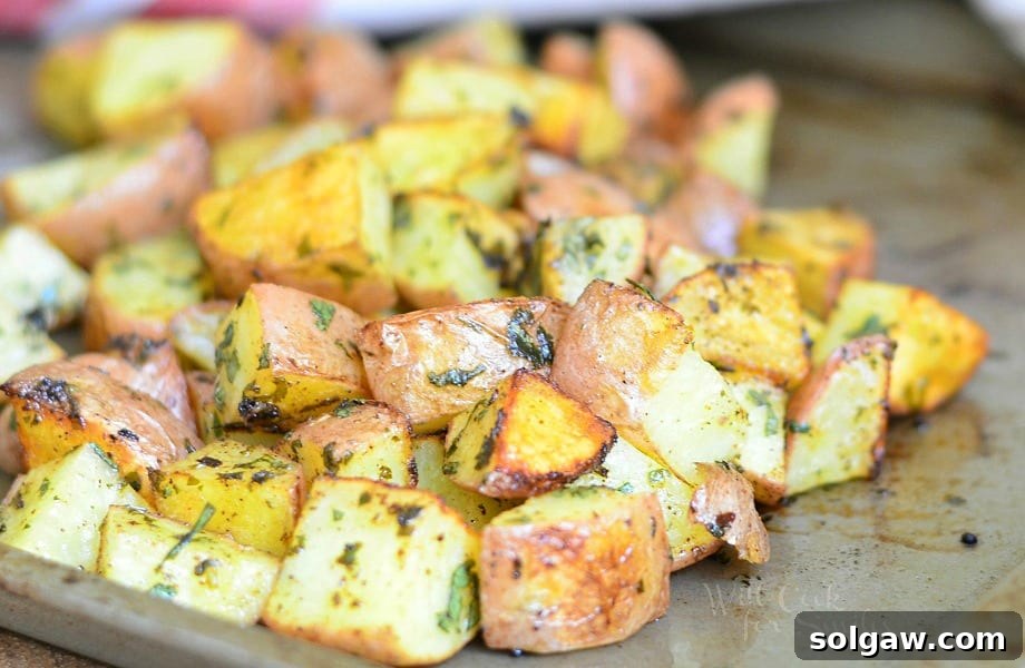 close up view of oven roasted potatoes cooked on a metal sheet tray presented on a wooden table with a white cloth with red stripes in background