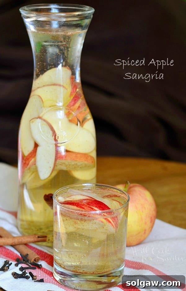 A pitcher of Spiced Apple Sangria with apple slices and cinnamon sticks, alongside a glass filled with the cocktail and apple garnishes.