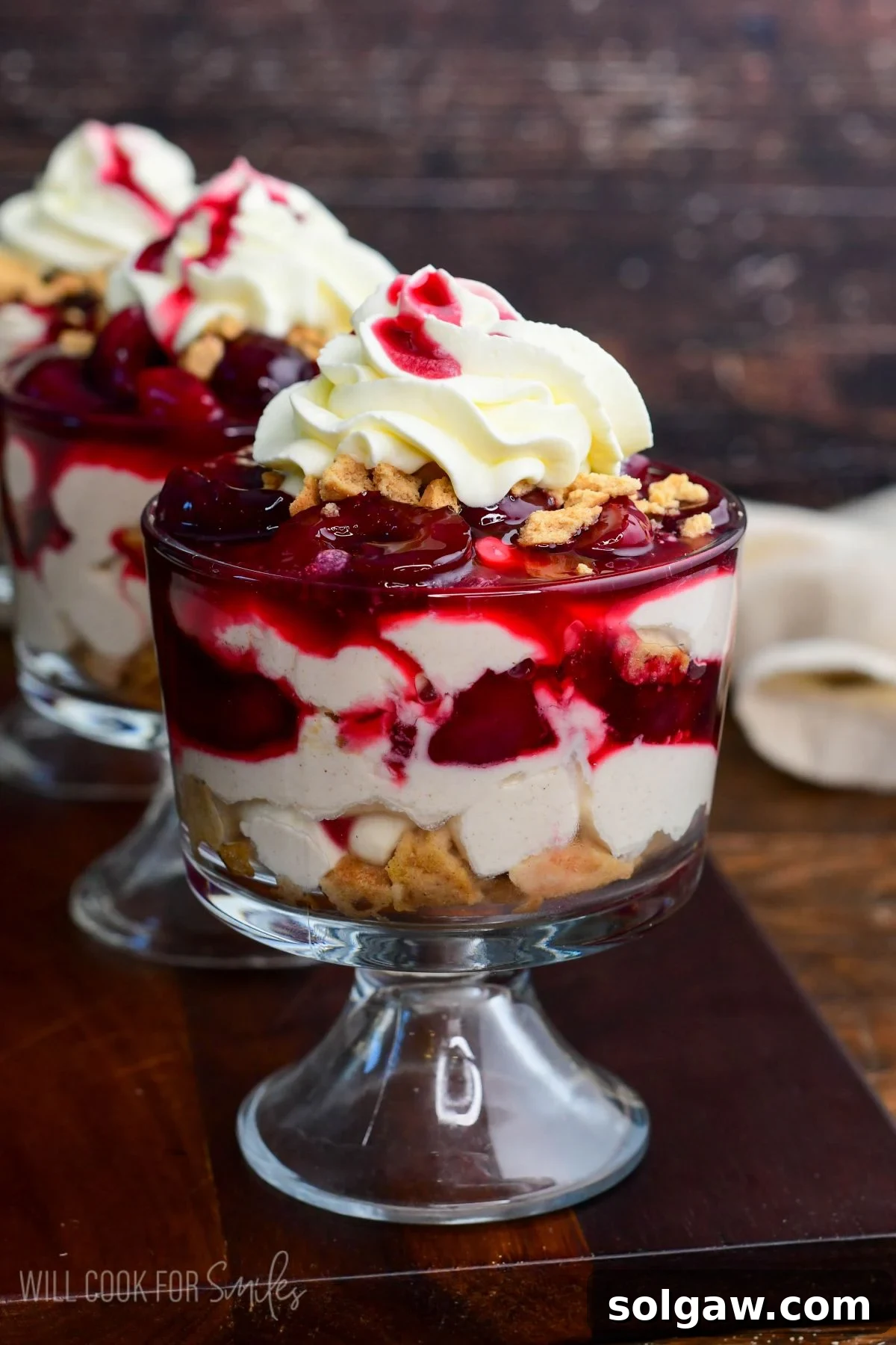 A vibrant no-bake cherry cheesecake parfait, beautifully layered with creamy cheesecake filling, crushed cookies, and luscious cherry sauce, crowned with fluffy whipped cream in a clear glass dessert cup.