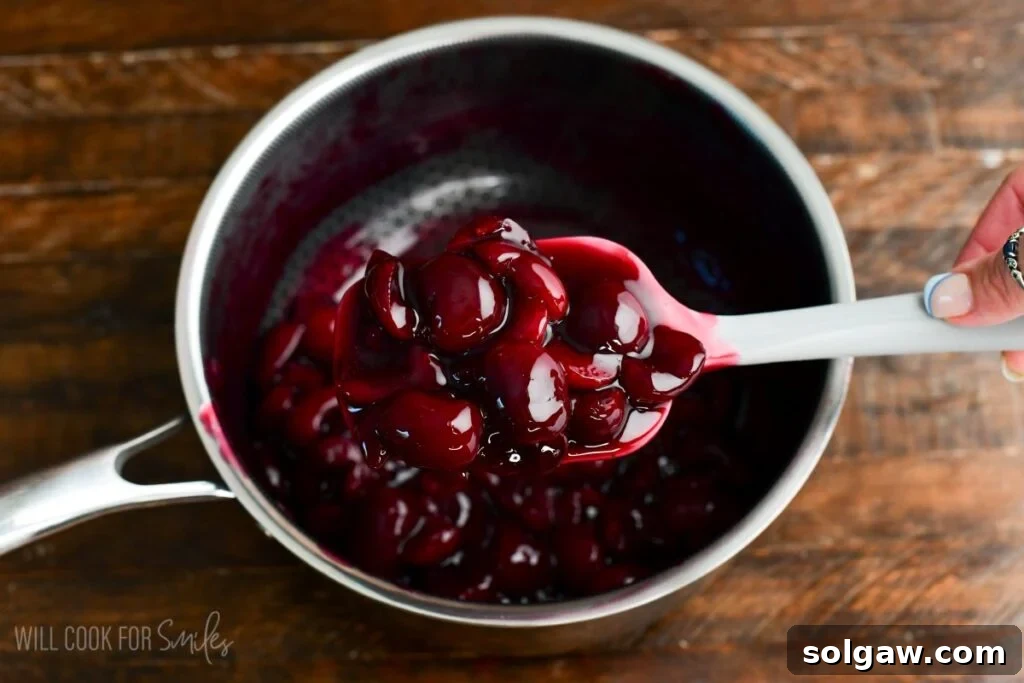 Homemade cherry topping being stirred in a saucepan, cooking down to a rich, syrupy consistency for the no-bake cherry cheesecake parfaits.