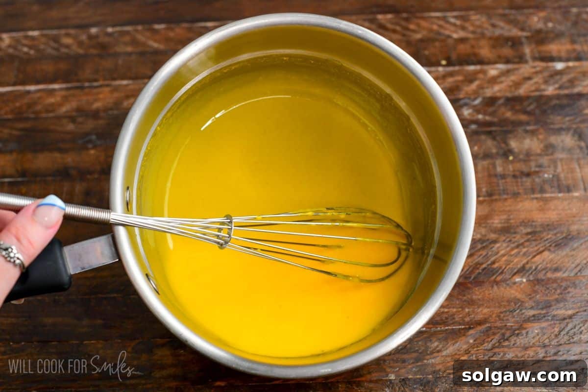 Velvet Pistachio Tiramisu 6 Tempered egg yolk mixture being whisked in a small saucepan, creating a smooth yellow custard base.