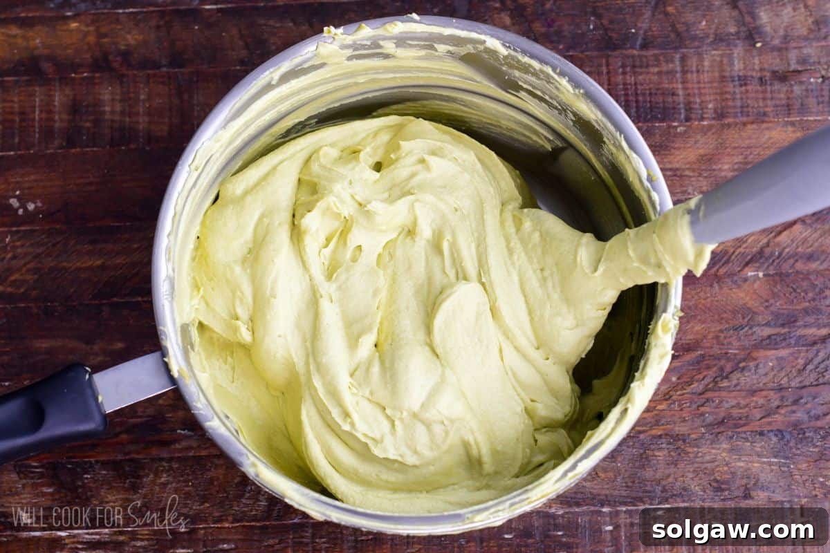 Velvet Pistachio Tiramisu 10 Smooth pistachio mascarpone cream mixture in a saucepan being stirred with a spatula for pistachio tiramisu filling.