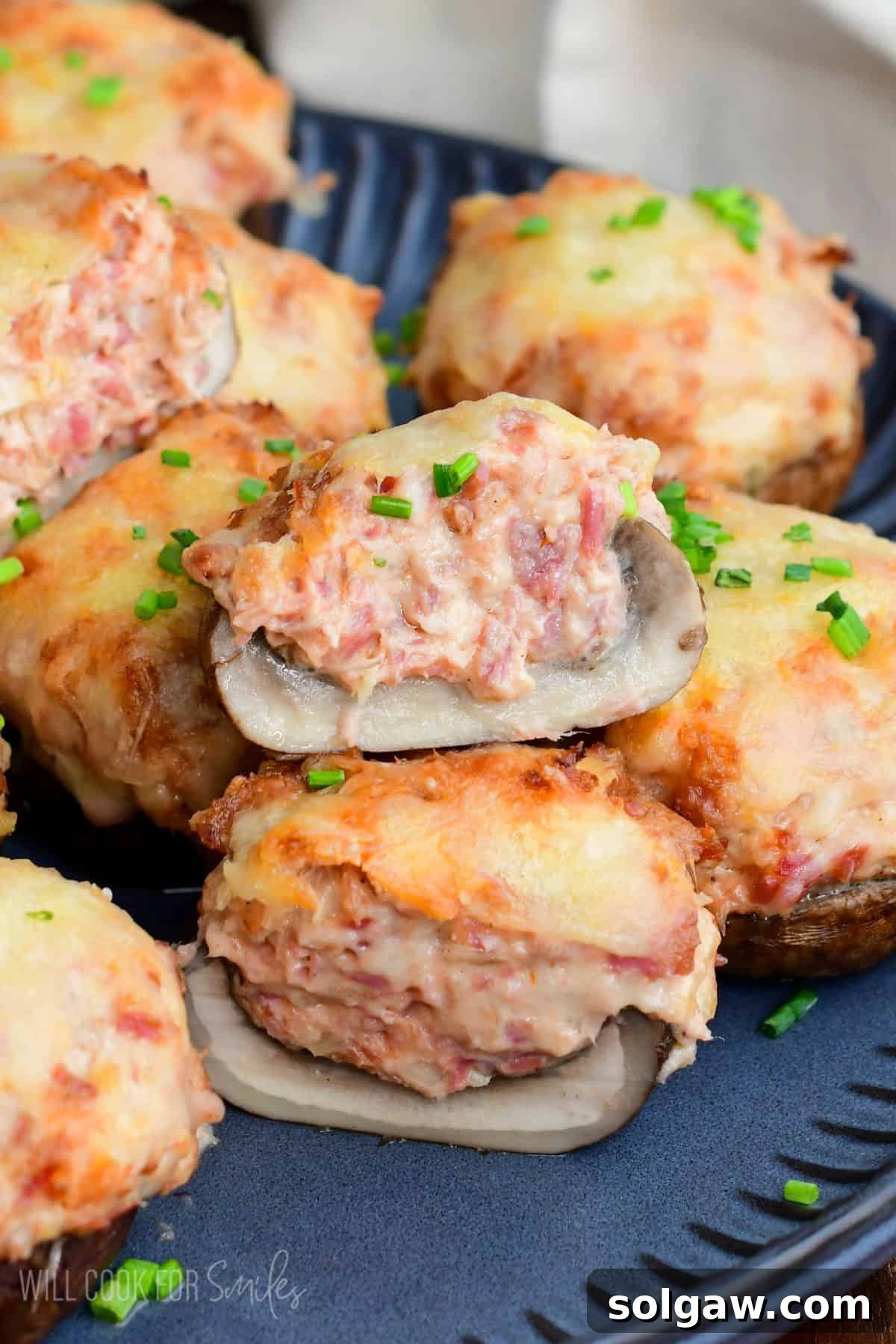 two halves of Reuben stuffed mushrooms topped with melted Swiss cheese and chives, stacked to show the creamy corned beef filling.