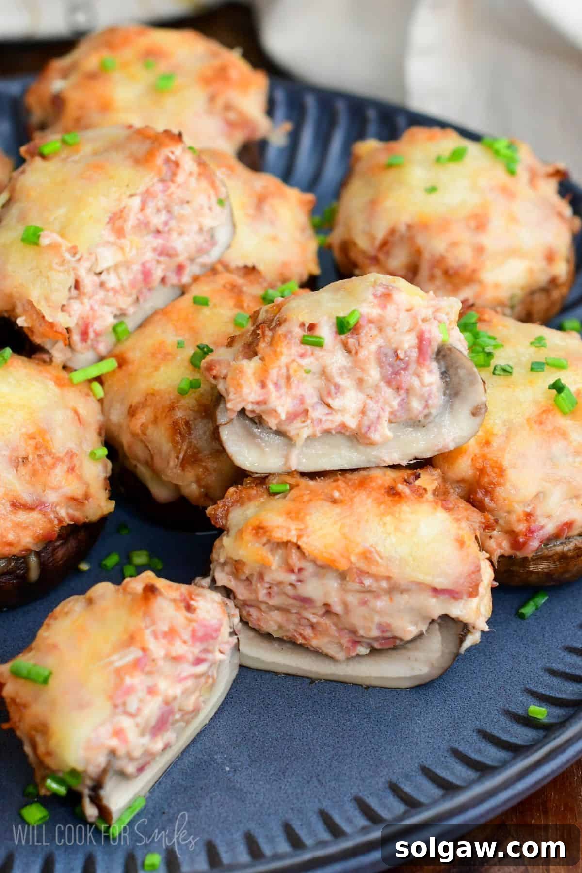 Close-up of Reuben stuffed mushrooms with melted Swiss cheese and chopped chives, one mushroom cut open to show the creamy corned beef filling.