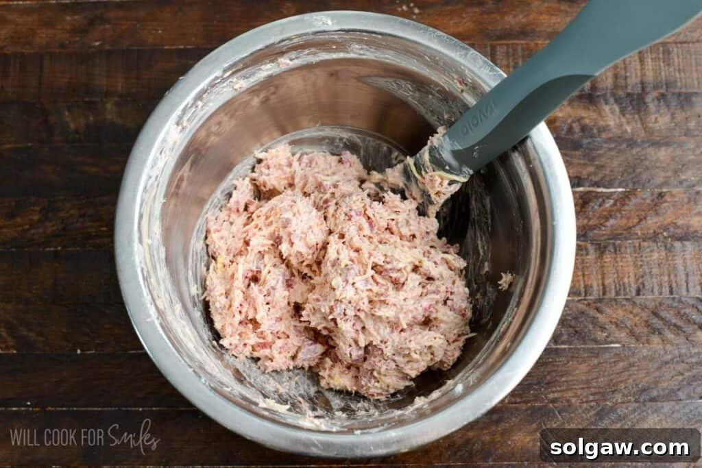 Mixing bowl with chopped corned beef, shredded Swiss cheese, sauerkraut, cream cheese, and dressing for Reuben stuffed mushrooms.
