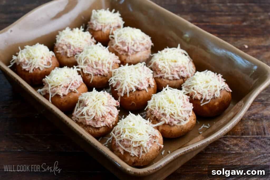 Baking dish filled with mushroom caps stuffed with creamy Reuben filling and topped with shredded Swiss cheese before baking.