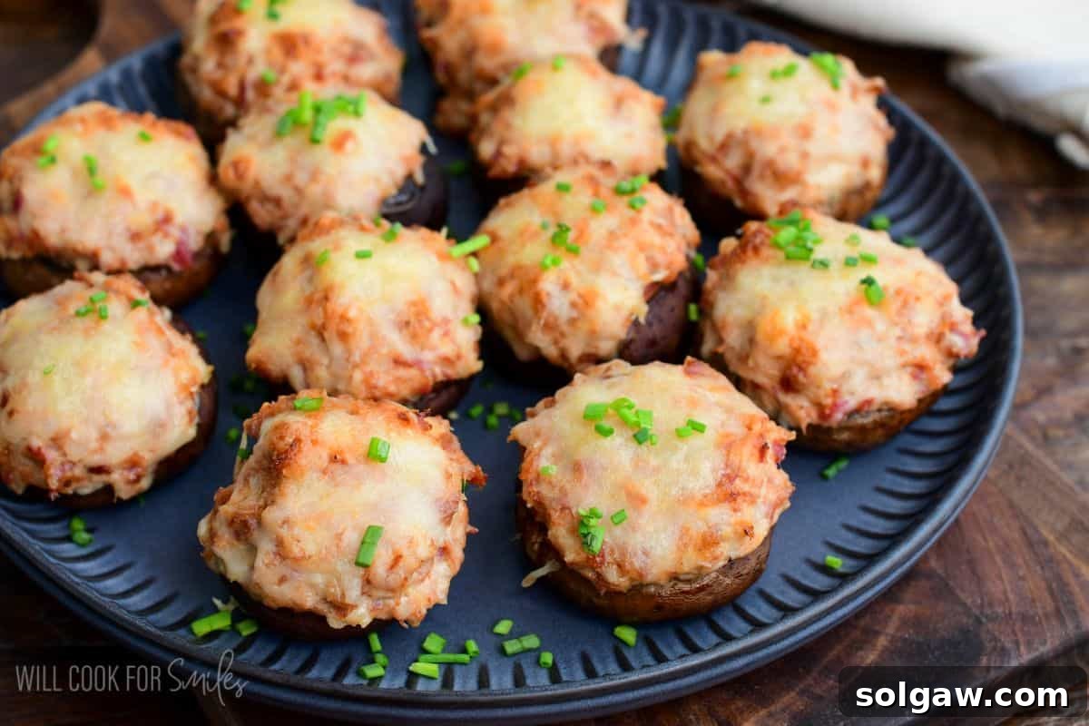 Reuben stuffed mushrooms topped with melted Swiss cheese and sprinkled with chopped chives, served on a dark platter.