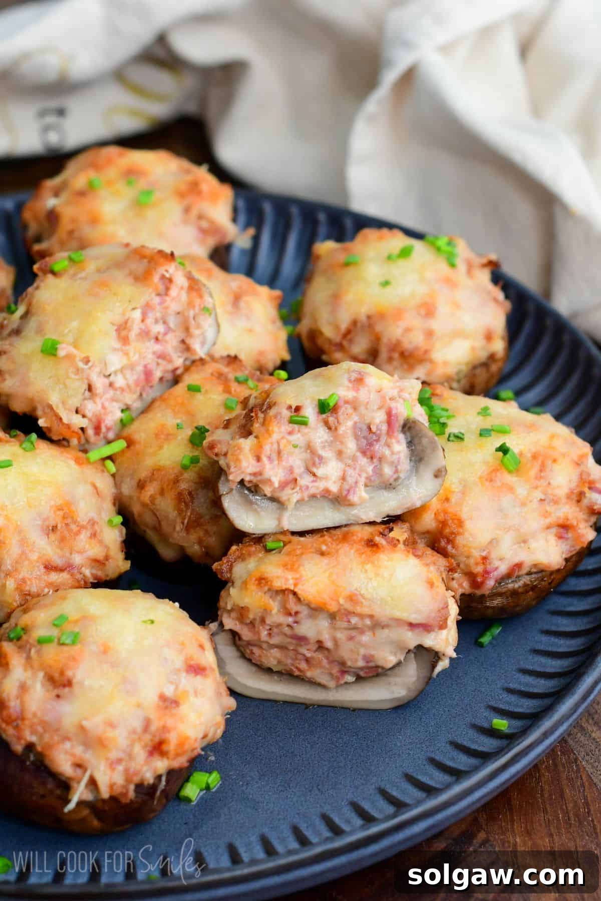 Reuben stuffed mushrooms with melted Swiss cheese and chives on a platter, with one cut open to reveal the creamy corned beef filling.