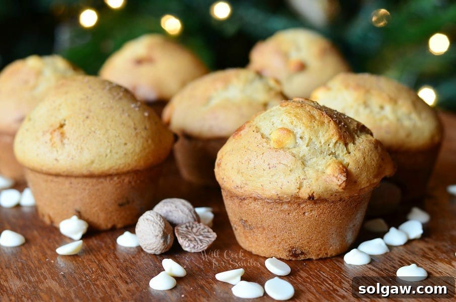 White Chocolate Chip Eggnog Muffins on a table with scattered white chocolate chips and whole nutmeg
