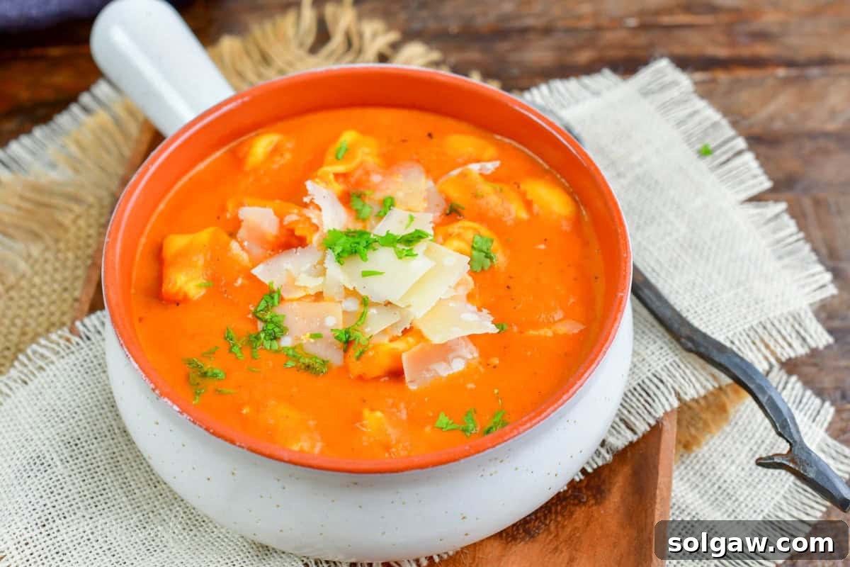 Velvety Roasted Red Pepper Tortellini Soup 7 A visually appealing bowl of roasted red pepper soup, elegantly placed on a wooden plate with a spoon resting beside it, ready to be enjoyed.