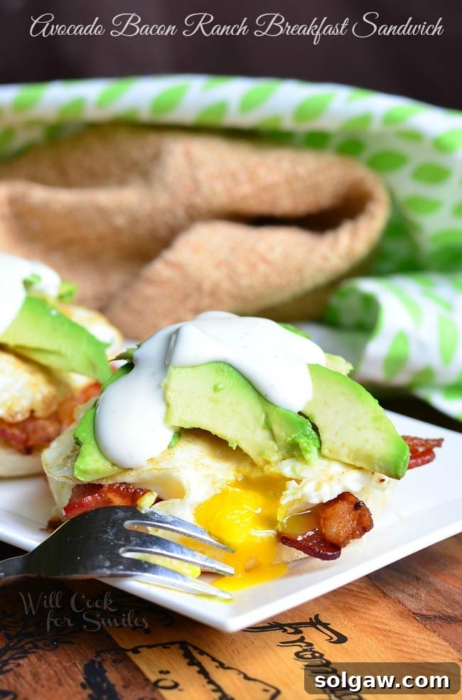 A vibrant close-up of the ultimate Avocado Bacon Ranch Breakfast Sandwich, showcasing fresh avocado, crispy bacon, a perfectly fried egg, and creamy ranch on a toasted English muffin.