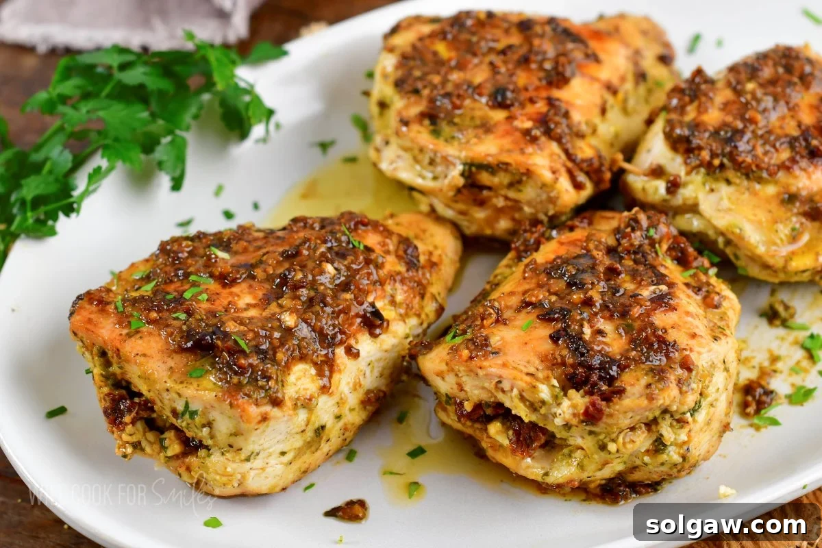 Feta Sun-Kissed Chicken 6 closeup of four pesto stuffed chicken breasts on a plate, garnished with fresh herbs.