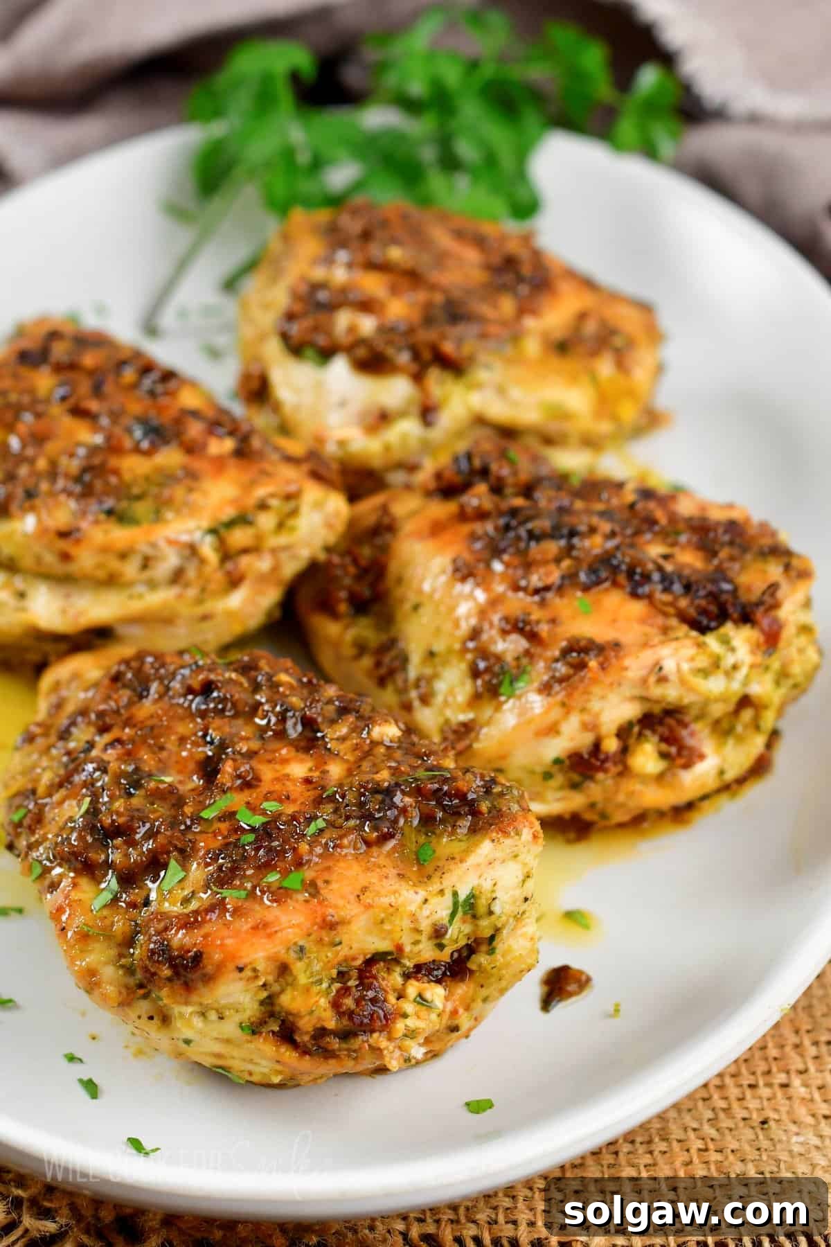 Feta Sun-Kissed Chicken 7 four pesto tomato stuffed chicken breasts on a platter, garnished with fresh basil leaves.