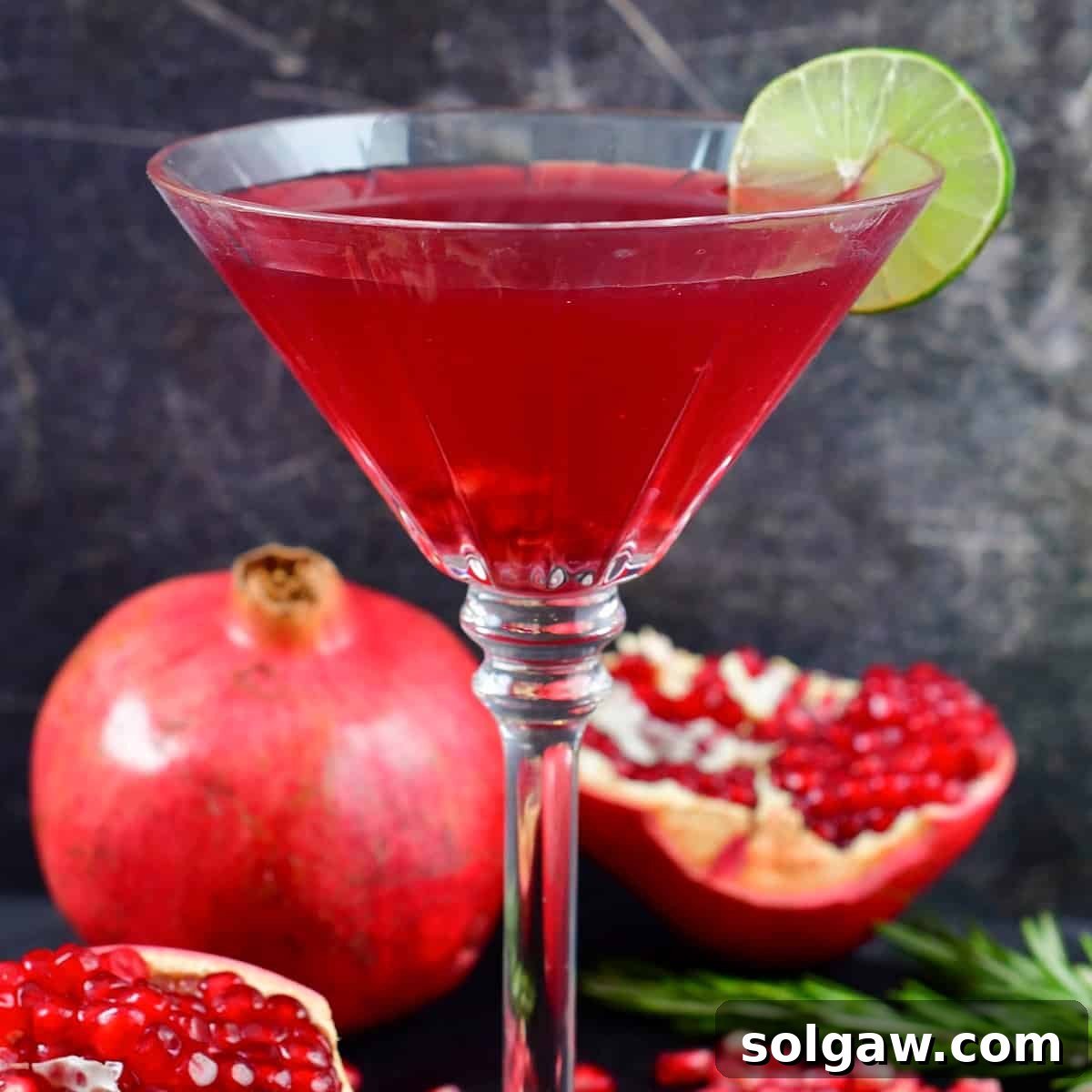 Centered image of a bright red cocktail in a martini glass, garnished with pomegranate seeds.