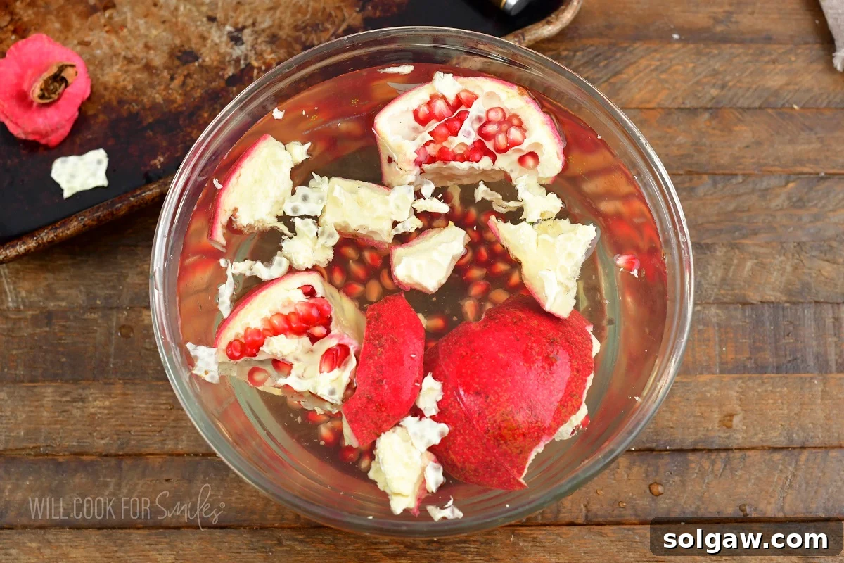 Pomegranate pieces submerged in a bowl of cold water, showing seeds being separated.
