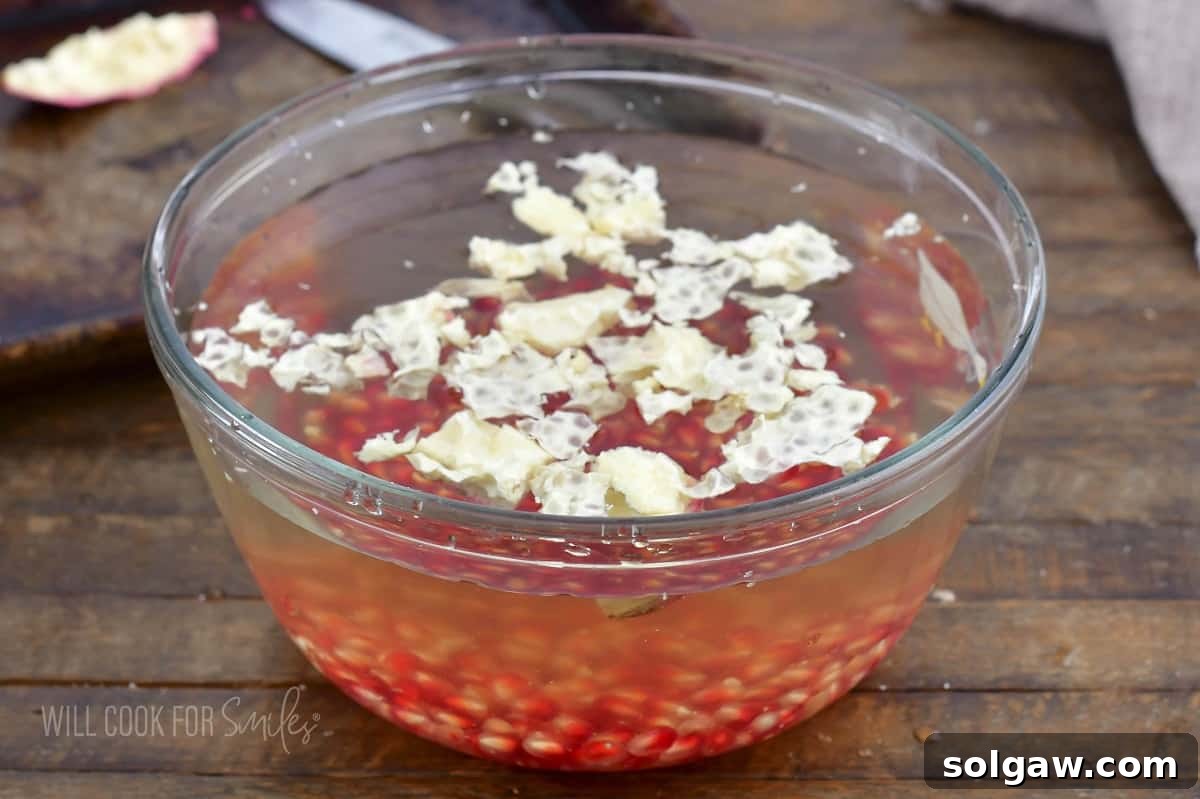 Clean pomegranate seeds settled at the bottom of a bowl of water, with membranes floating.