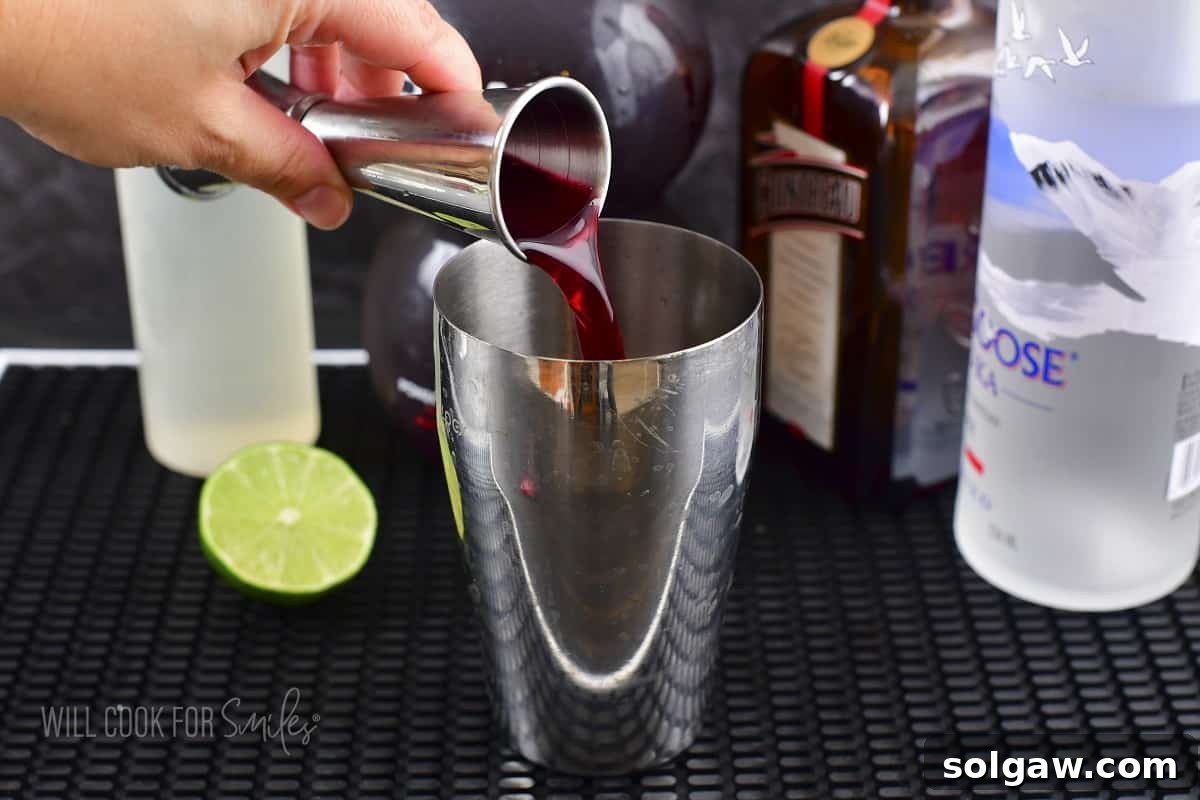 Pomegranate juice being poured into a cocktail shaker filled with ice.