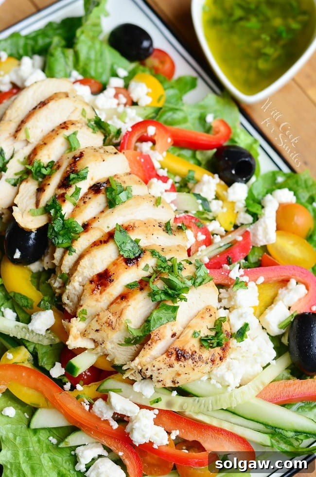 sliced chicken bread on top of a Greek salad with dressing next to the plate