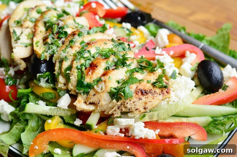 Close-up view of a white rectangular plate with a black rim, featuring a Greek chicken salad on a wooden table, emphasizing the fresh ingredients.