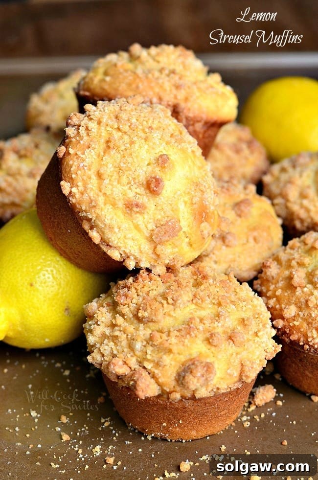 Piled Lemon Streusel Muffins with fresh lemons on a wooden surface.