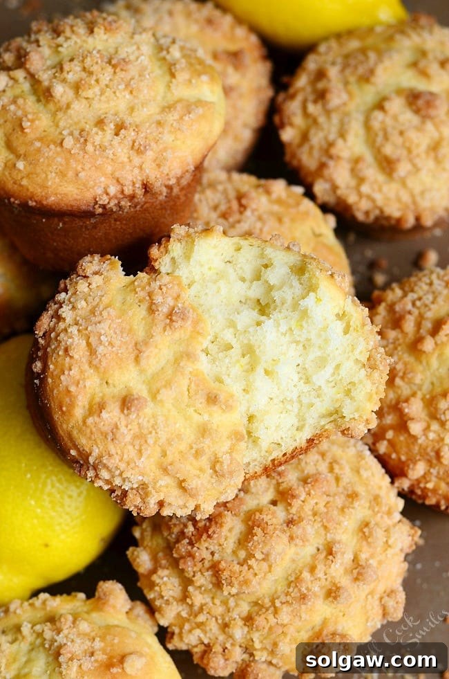 A stack of golden Lemon Streusel Muffins on a white plate, with a fresh lemon cut in half next to them.