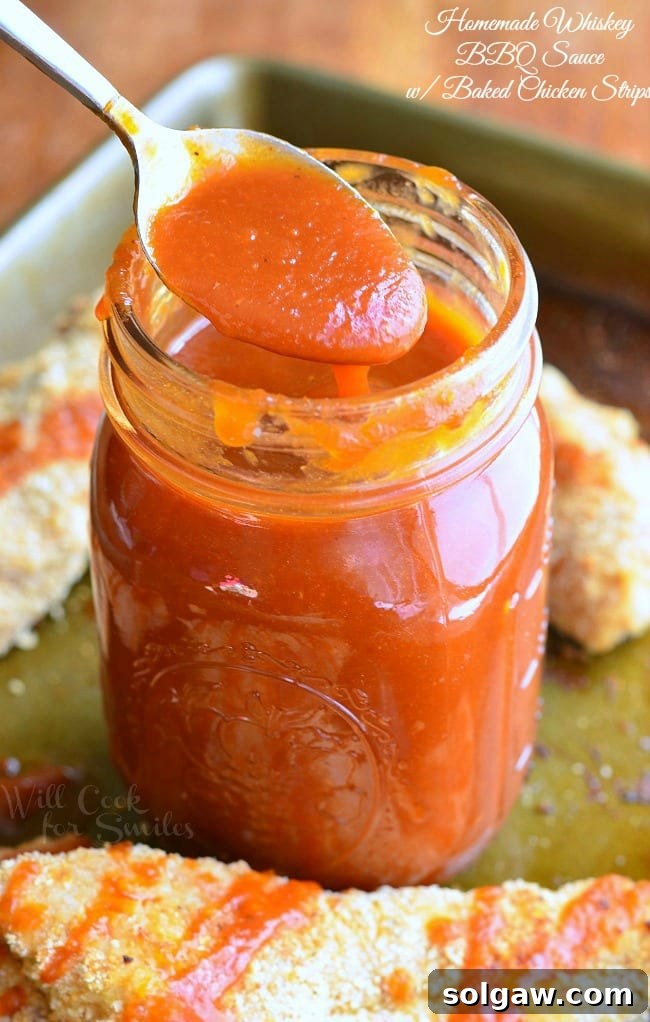 A mason jar filled with rich, Homemade Whiskey BBQ Sauce, with a spoon gently scooping some out, highlighting its delicious texture.
