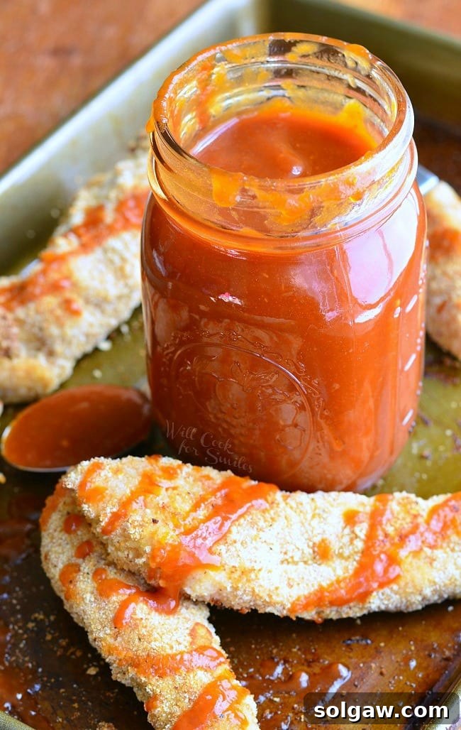 A beautifully arranged scene featuring a mason jar of Whiskey BBQ Sauce next to a baking sheet laden with golden-brown, crispy Chicken Strips, ready for dipping.