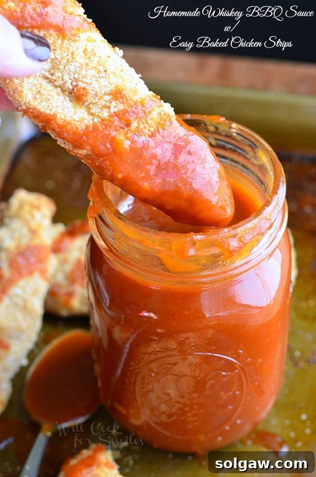 A delicious chicken strip being dipped into the rich, Homemade Whiskey BBQ Sauce in a mason jar, showcasing the perfect bite.