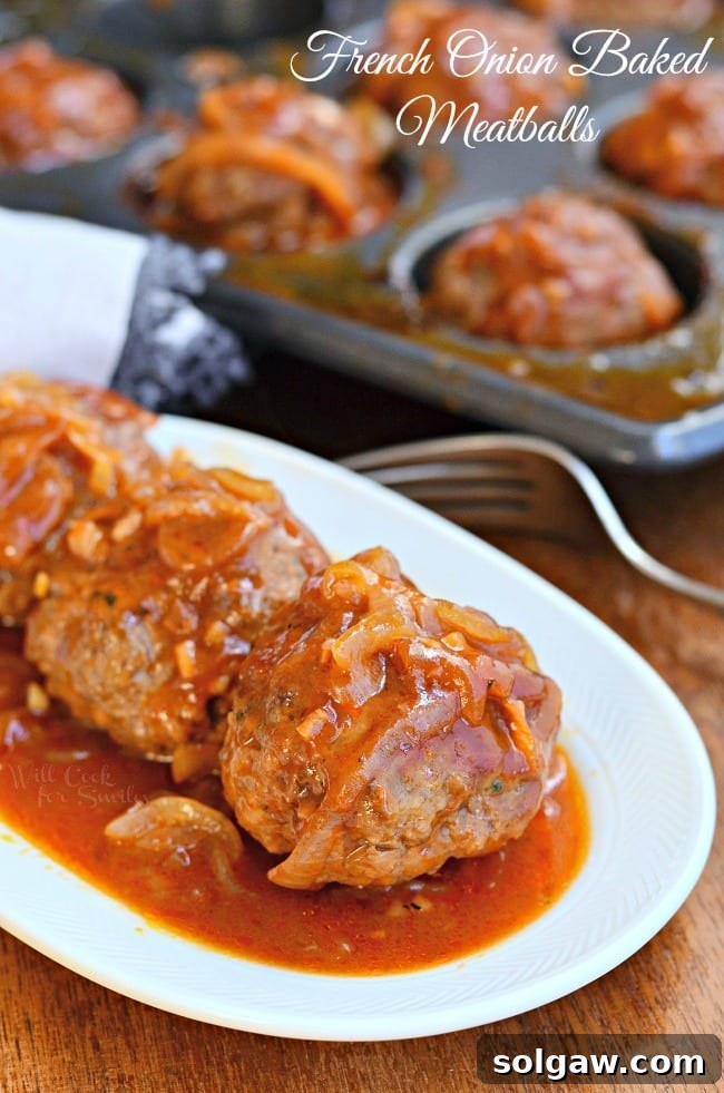small white oval dish with french onion baked meatballs on a wooden table with a fork and cupcake baking pan filled with additional meatballs in it in background.
