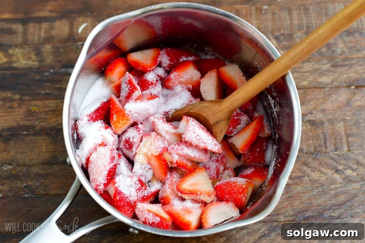 Chopped strawberries in a saucepan with granulated sugar sprinkled over them, ready to cook.