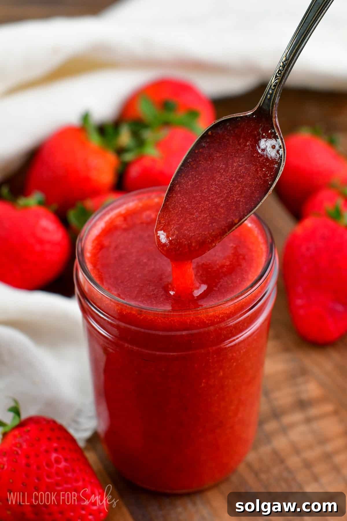 A small spoon scooping vibrant strawberry sauce out of a glass jar, highlighting its rich color and texture.