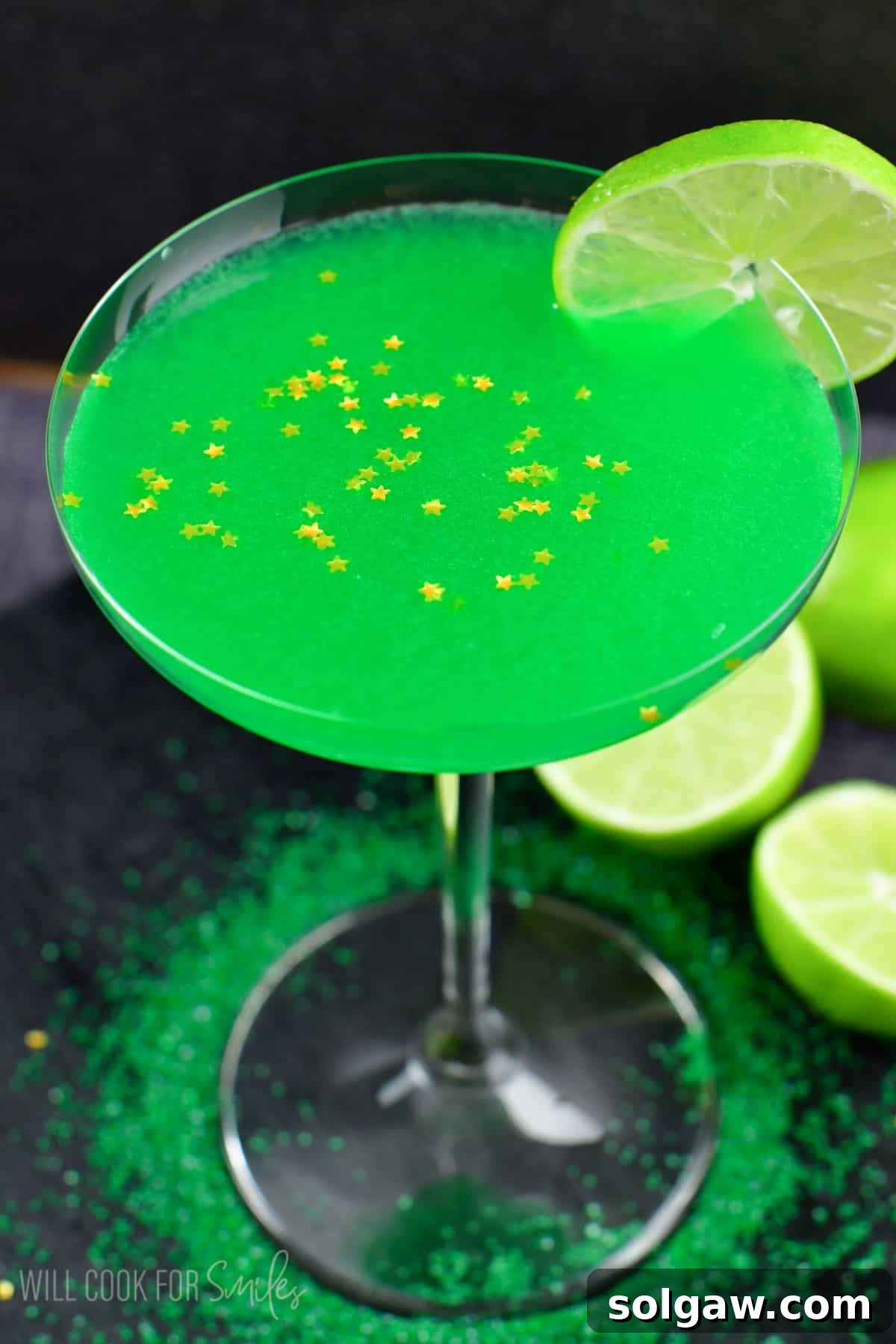 A vibrant green lime martini in a classic martini glass, garnished with a fresh lime slice on the rim and delicate gold star sprinkles on the surface.