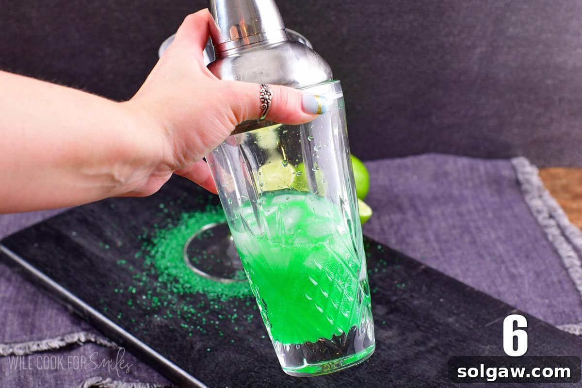 A cocktail shaker being vigorously shaken to mix the lime martini ingredients with ice, creating a chilled and well-combined drink.