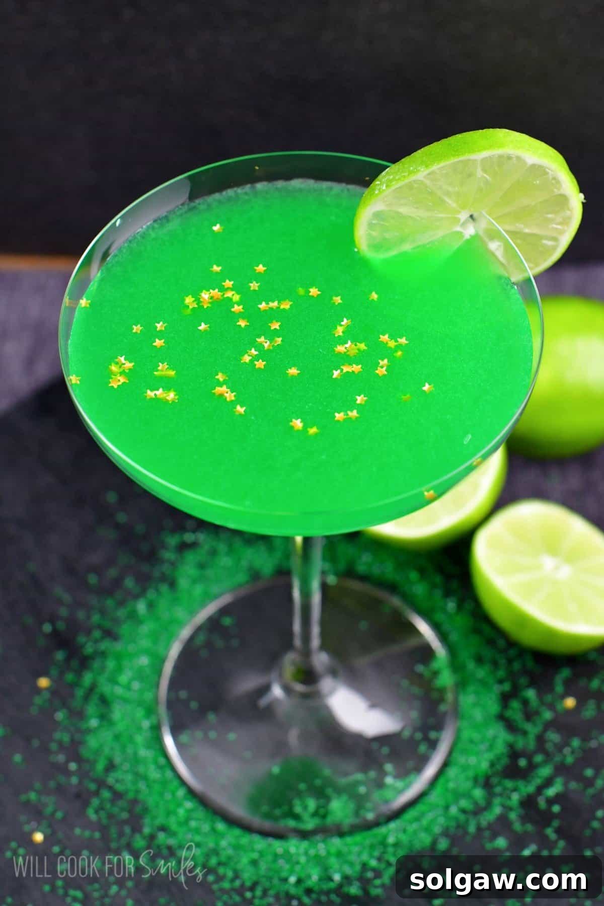 A refreshing green martini served in a classic martini glass, adorned with a lime slice on the rim and star-shaped sprinkles.