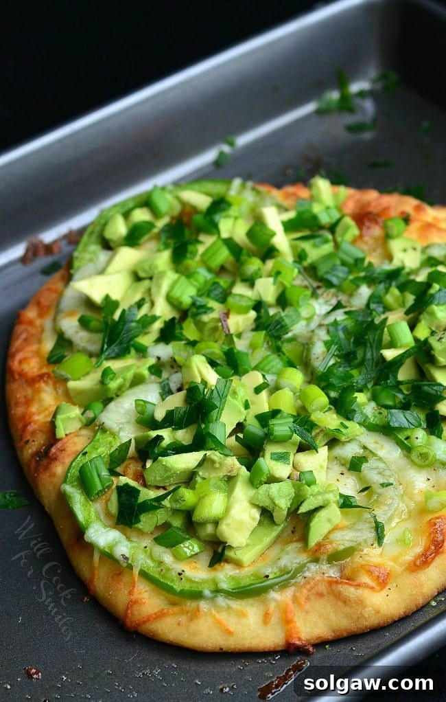 Green Naan Pizza with avocado, green peppers and green onions on top, served on a cutting board.