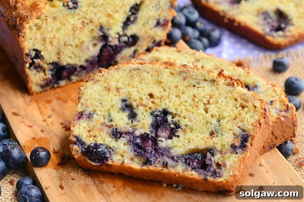 Toasted Coconut Blueberry Bread sliced on a cutting board with fresh blueberries scattered around