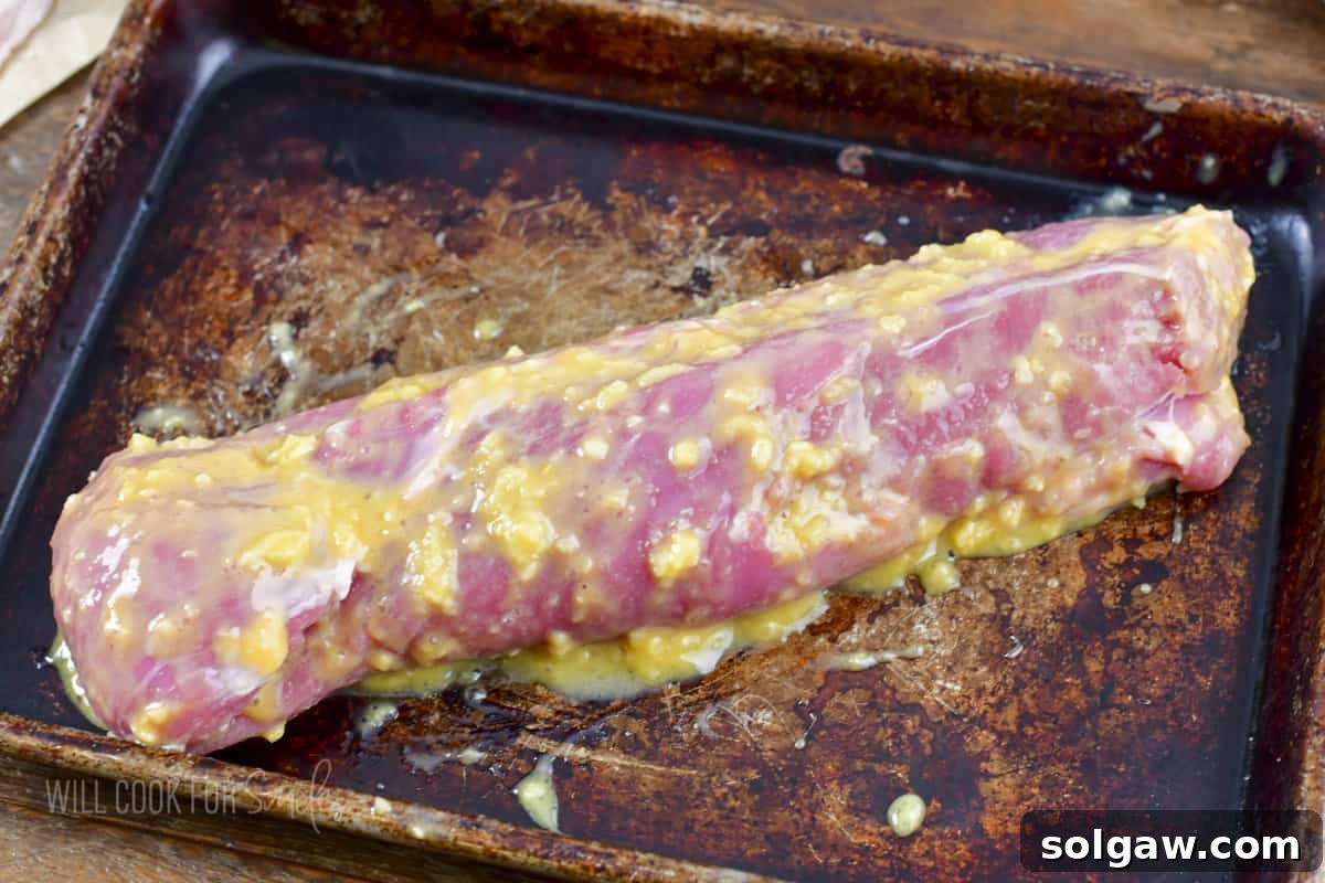 Bacon Wrapped Pork Perfection 5 Pork tenderloin being coated evenly with a generous layer of Dijon mustard and garlic rub.