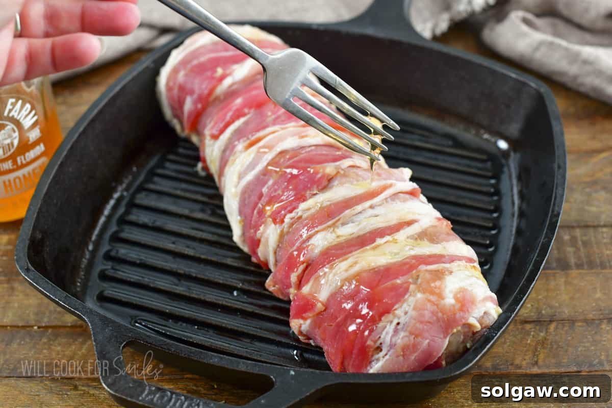 Bacon Wrapped Pork Perfection 7 Honey being drizzled over the bacon wrapped pork tenderloin before baking.