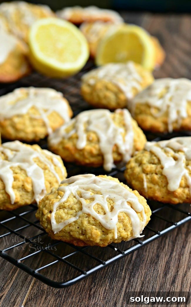 Soft oatmeal cookies with a lemon vanilla glaze resting on a wire cooling rack, glistening under soft light. Some cookies are topped with extra lemon zest.