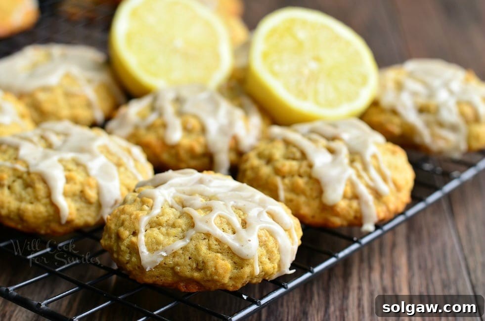 Oatmeal cookies with a glistening lemon glaze arranged neatly on a cooling rack, ready to be enjoyed. Halved lemons are scattered around for decoration.