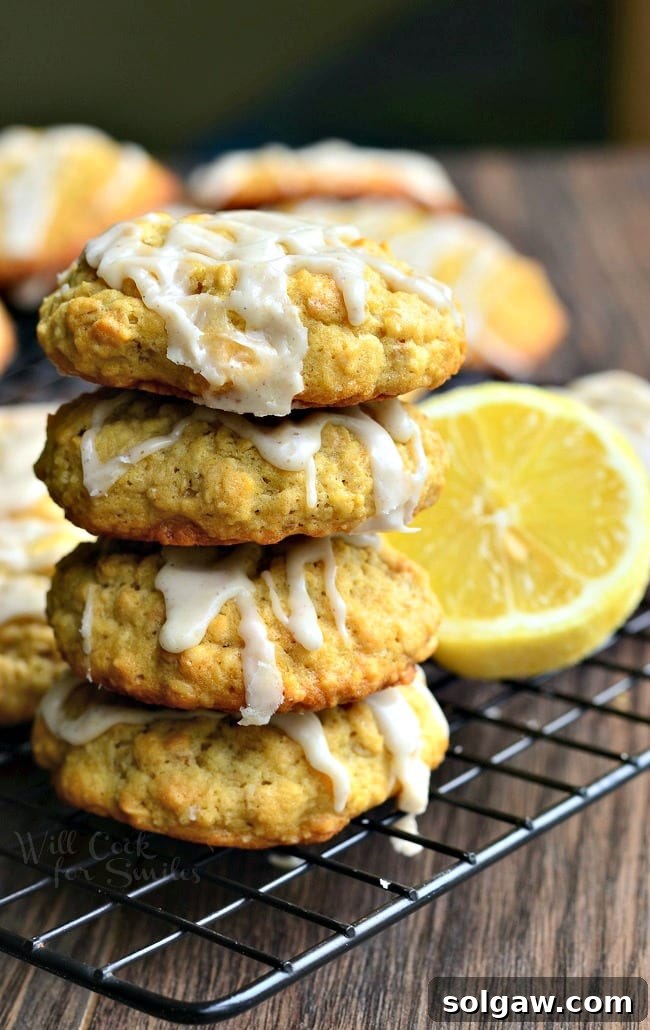 A close-up of soft lemon vanilla glazed oatmeal cookies stacked on a cooling rack, with a few fresh lemon slices nearby.