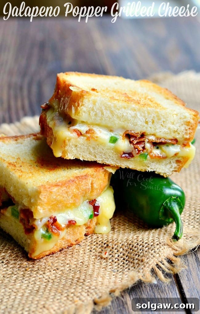 Jalapeno Popper Grilled Cheese loaded with gooey cheese, jalapenos and bacon cut in half with a jalapeno to the side 