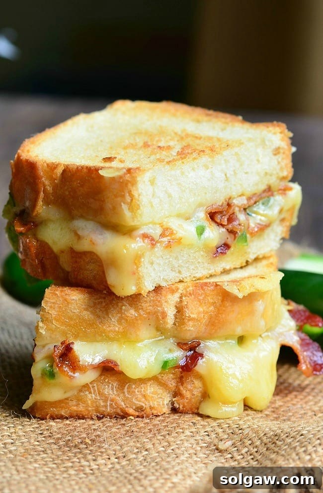 Jalapeno Popper Grilled Cheese loaded with gooey cheese, jalapenos and bacon cut in half with a jalapeno to the side 