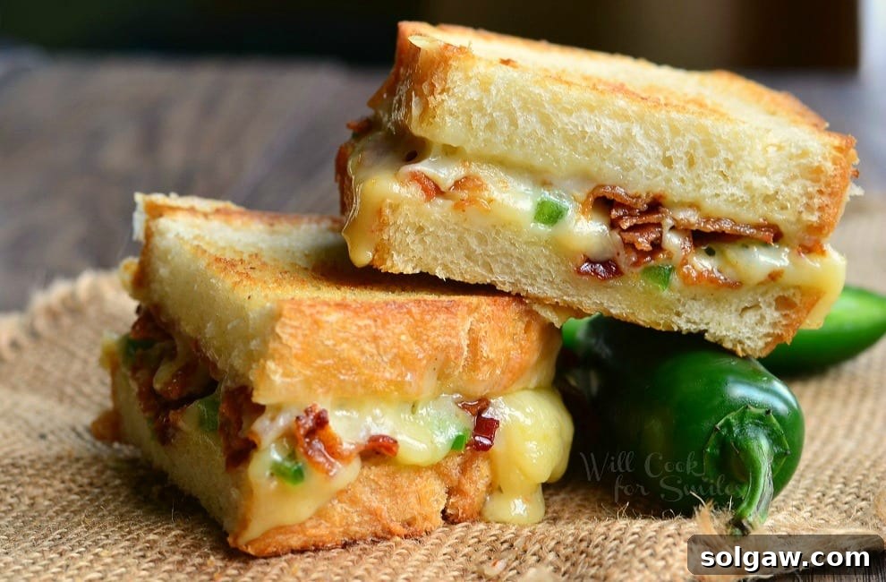 Jalapeno Popper Grilled Cheese loaded with gooey cheese, jalapenos and bacon cut in half with a jalapeno to the side 