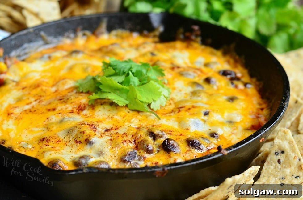 Hot 7 Layer Dip with cheese and black beans in a cast iron skillet with cilantro on top as garnish and tortilla chips around the pan