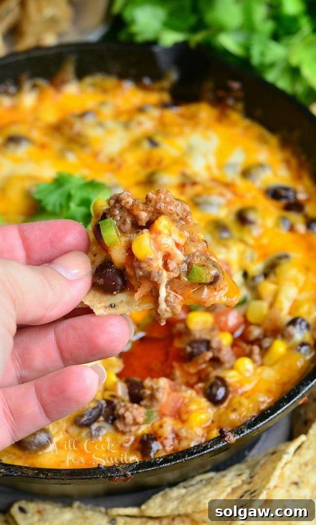 Dipping a chip into the Hot 7 Layer Dip with ground beef, corn, and black beans on it
