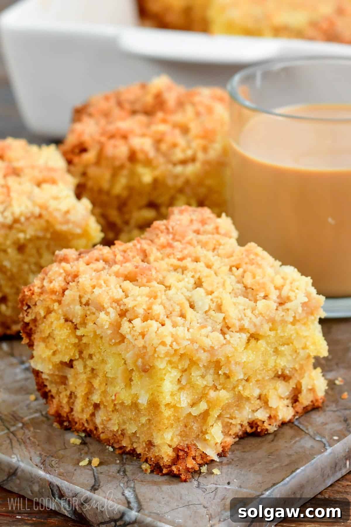 Slice of coconut coffee cake with a glass of coffee next to it.