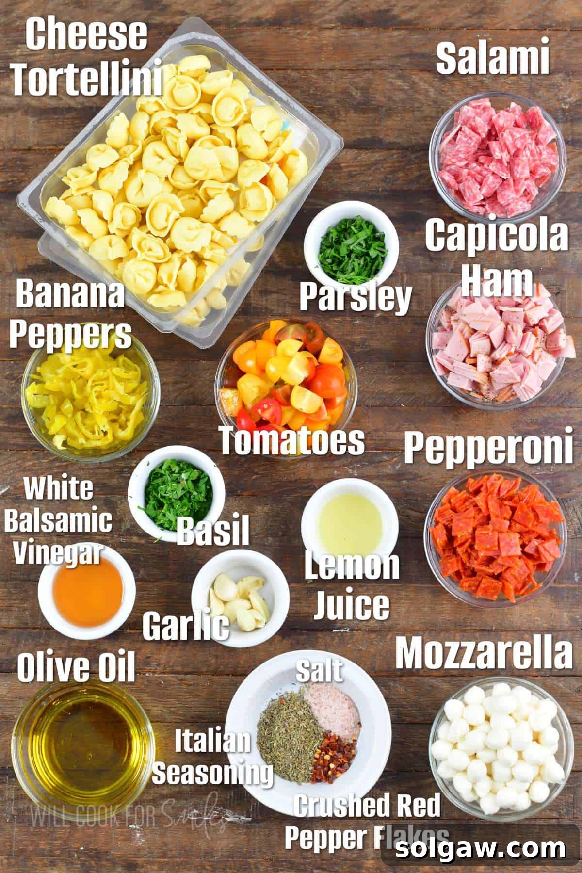 labeled ingredients to make Italian tortellini salad on a wooden board. Fresh, vibrant ingredients laid out for preparation.